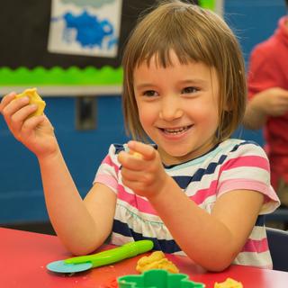3K student playing with playdough at red table